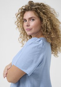 Haut bleu clair à manches courtes en tissu texturé avec un col rond. Présente des accents froncés aux épaules.