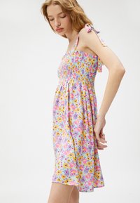 Vestido de tirantes con smock en púrpura claro con un estampado floral en amarillo, rosa y azul. Presenta tirantes con lazo y una falda acampanada.