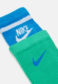 Nike-Socken mit einem blauen Rippmuster, weißen Streifen und Logo sowie einem grünen Abschnitt mit einem blauen Logo, aus strukturiertem Strickmaterial gefertigt.