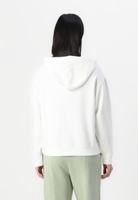 Hvit hettegenser med en myk tekstur, med hette og ribbestrikkede mansjetter, sammen med lysegrønne joggebukser. Enkelt og minimalistisk design.