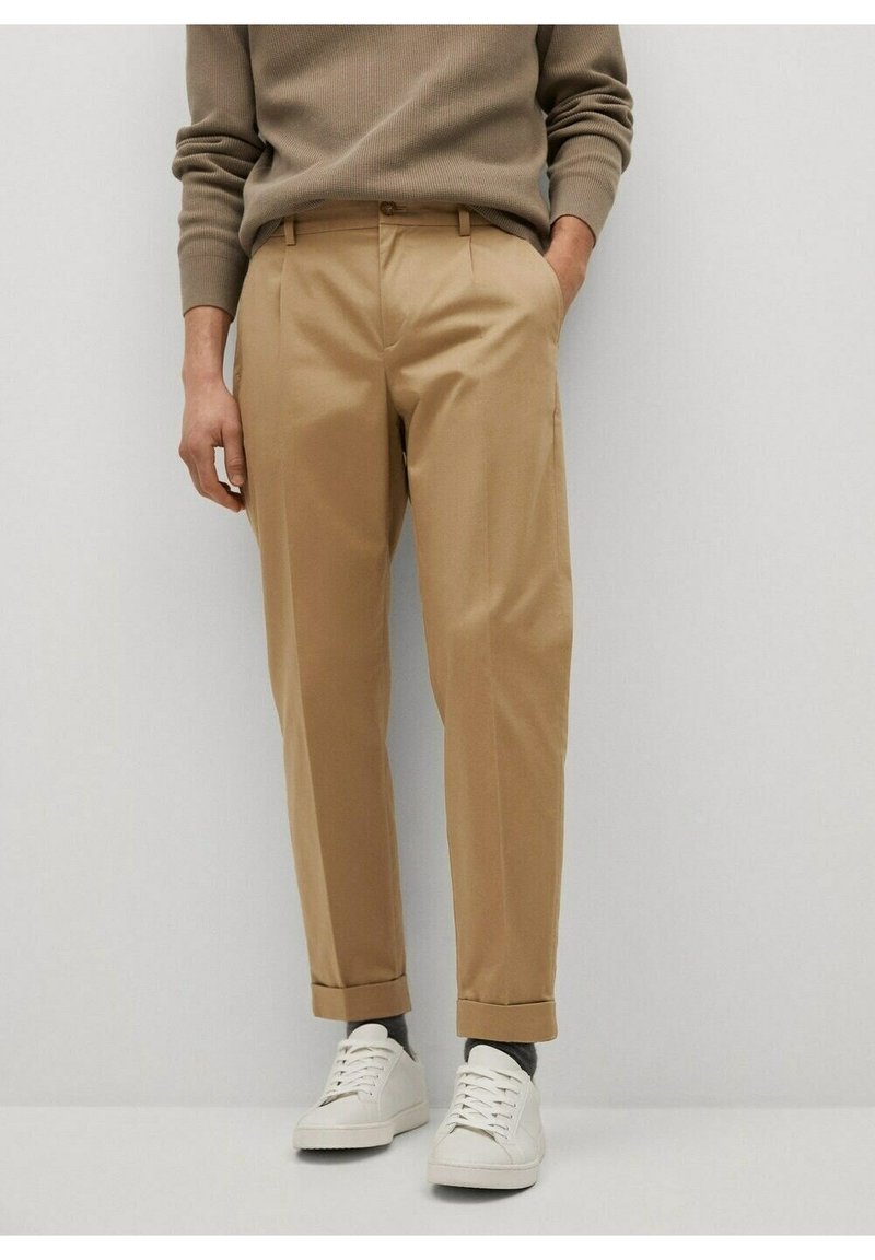 Beige op maat gemaakte broeken met een gladde textuur, voorzien van zijzakken, voorkruissingen, omgeslagen zoom, gecombineerd met witte sneakers.