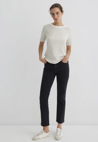 Gestreifte Baumwoll-T-Shirt mit kurzen Ärmeln, weiß-beige Streifen. Kombiniert mit dunklen Denim-Jeans und weißen sowie grauen Low-Top-Sneakern.