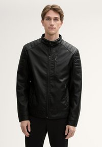 Giacca di pelle nera con colletto alto, accenti trapuntati sulle spalle, chiusura frontale con zip e due tasche laterali. Dettagli a coste sulle maniche.