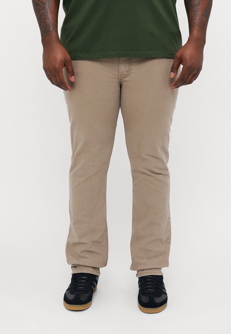 Pantalons en coton beige avec une coupe droite, associés à des sneakers noires avec un dessus texturé et une semelle en caoutchouc gomme.