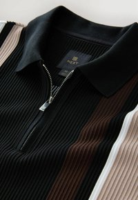 Svart och randig halvdraget polotröja med ribbad textur. Har bruna, vita och beige ränder. Silvrig dragkedja och varumärkeslogotyp synlig.