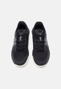 Para czarnych sportowych tenisówek z białymi podeszwami, siateczkową tkaniną i sznurowadłami, widzianych z góry na białym tle.