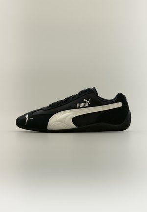 Baskets Puma noires avec logo Puma blanc et bande latérale, design profil bas et lacets noirs sur fond neutre.