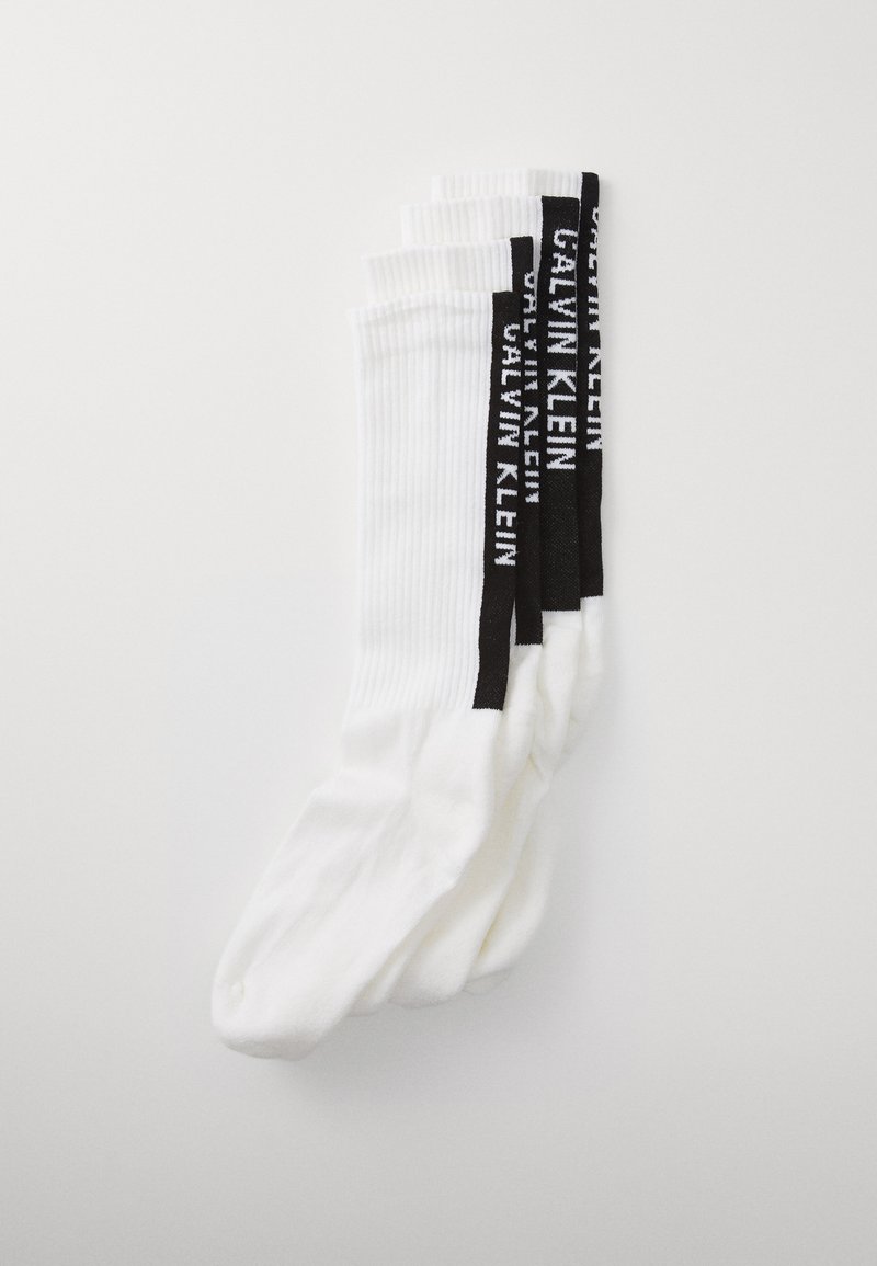 Τέσσερις ζεύγη κάλτσες από βαμβακερό μείγμα: δύο λευκές με ραβδωτή υφή, δύο μαύρες με τη γραφή "Calvin Klein" σε λευκό κατακόρυφο κείμενο.