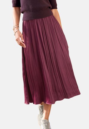 Plissee-Midirock in sattem Pflaumenton, mit vertikalen Falten, elastischem Bund und fließendem Schnitt, kombiniert mit hellgrauen Sneakers.