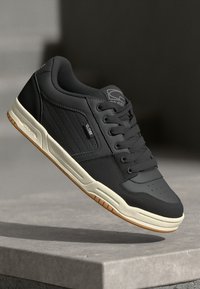 Black sneaker with a smooth leather upper, perforated details, white midsole, and a gum rubber outsole. Features lacing and branding accents.