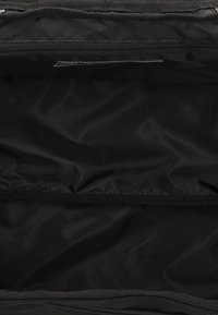 Interno di una borsa in nylon nera con texture liscia, dotato di un compartimento con zip e una tasca aggiuntiva per l'organizzazione.