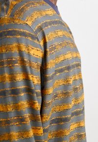 Gray fabric top featuring bold, horizontal stripes in yellow and brown. Textured surface with variations in pattern. Round neckline.