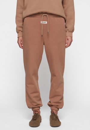 Brown cotton sweatpants with elastic cuffs, adjustable drawstring waist, and a woven brand label on the front. Soft texture, casual fit.