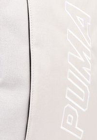 Gros plan sur un tissu blanc texturé avec le texte brodé blanc "PUMA" et la couture visible.