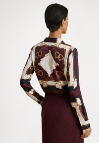 Μεταξωτή μπλούζα με σχέδιο αλυσίδας σε εκρού και βουργουνδί φόντο, μακριά μανίκια και δομημένο γιακά.