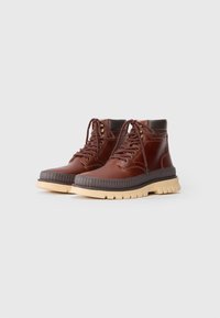 Bottines en cuir marron avec bout arrondi, col rembourré, semelle en caoutchouc épaisse et œillets en métal pour les lacets. Détails texturés sur la semelle.