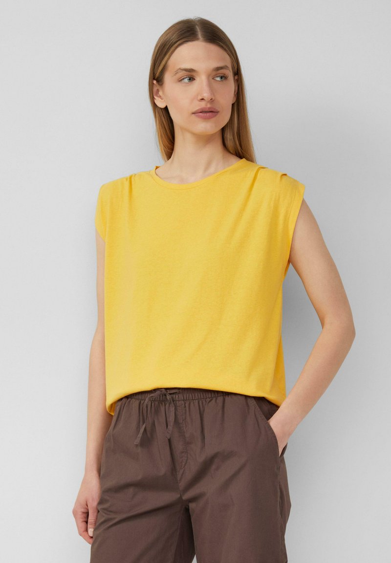 Yellow short-sleeve top made of soft fabric with a loose fit, featuring a round neckline and shoulder pleats. Paired with brown elastic waistband pants.