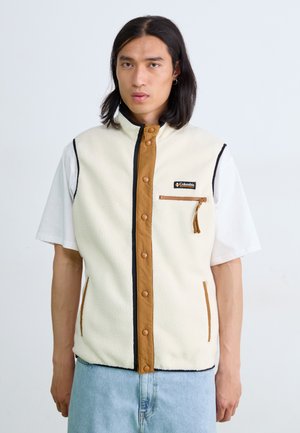 Fleece sleeveless vest in cream with brown front button closure, side pockets, and contrasting black trim; front zip pocket with tassel.