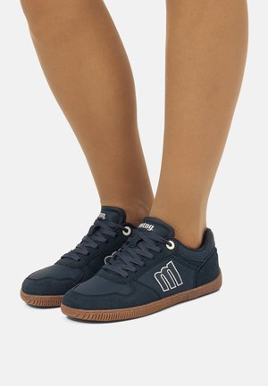 Zapatillas azul marino con acabado de ante, suela de goma y logo blanco. Presentan cordones redondos y un cuello acolchado para mayor comodidad.
