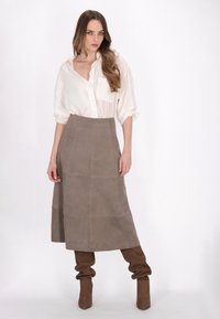 Hellgraues Button-Up-Hemd mit einer einzelnen Tasche, kombiniert mit einem knielangen taupefarbenen Wildledröcke und braunen, lässigen kniehohen Stiefeln.
