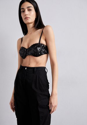 Melna spīdoša bralette ar regulējamiem plecu siksniņām, apvienots ar vaļīgām melnām kargo biksēm ar sānu kabatām un pogu aizdari.