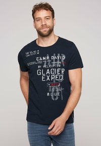 Camiseta de color azul marino con mangas cortas, que presenta texto gráfico en blanco y rojo y coordenadas. Tejido suave con un ajuste relajado.