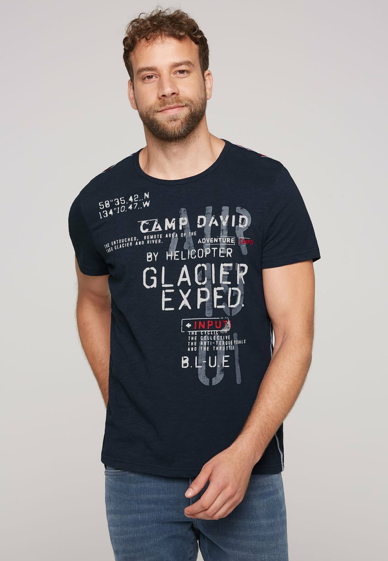 Camiseta de color azul marino con mangas cortas, que presenta texto gráfico en blanco y rojo y coordenadas. Tejido suave con un ajuste relajado.