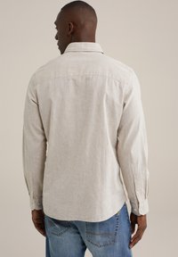 Light beige long-sleeve shirt with a textured fabric, featuring a pointed collar and buttoned cuffs, tucked into blue jeans.