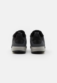 Zapatillas deportivas negras con parte superior de malla y suela de goma resistente. Presentan una lengüeta prominente en el talón y acentos texturizados para mayor agarre.