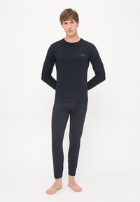 Haut à manches longues noir et pantalon ajusté en tissu lisse, avec un petit logo rouge sur la poitrine, design minimaliste et coupe près du corps.