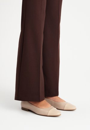 Ballerine in pelle beige con punta rotonda e dettaglio a cappuccio crema a contrasto, abbinate a pantaloni a gamba larga marroni.