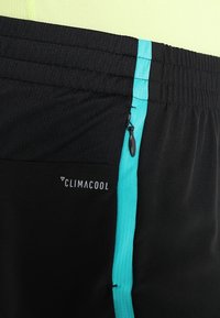 Pantalones cortos deportivos negros con una franja lateral turquesa, cinturilla elástica, marca CLIMACOOL y textura suave. Incluye un detalle de cremallera.