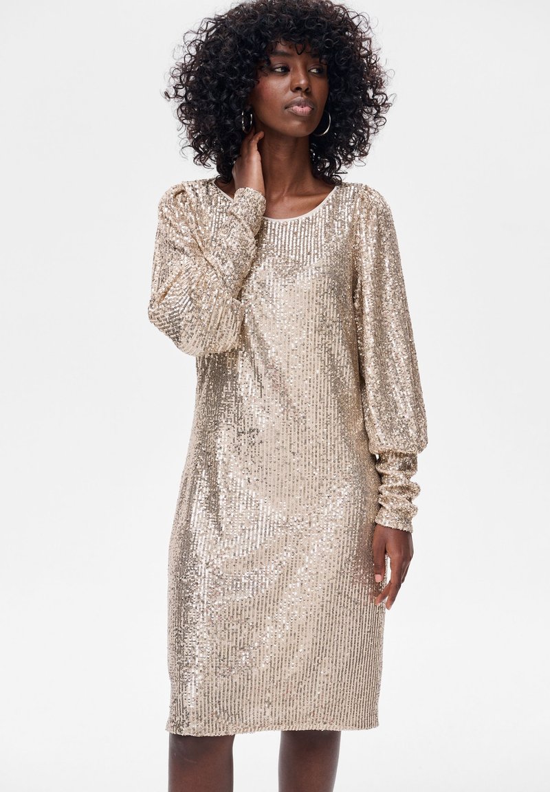 Błyszcząca sukienka z złotych cekinów z długimi bufiastymi rękawami i zaokrąglonym dekoltem, o prostej sylwetce i gładkiej fakturze.