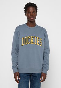 Felpa grigia a girocollo realizzata in cotone misto, con la scritta gialla "DICKIES" in caratteri grandi sul petto, rifinita con polsini e orlo a costine.
