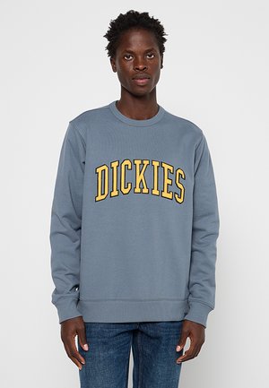 Grey crewneck sweatshirt made of cotton blend, featuring bold yellow text "DICKIES" across the chest, finished with ribbed cuffs and hem.