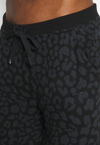 Pantalones jogger negros con un patrón de estampado de leopardo oscuro, cinturilla elástica con cordón y un pequeño logo de Nike en la parte frontal.