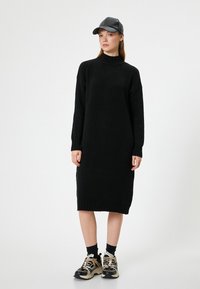 Abito nero lavorato a maglia con colletto alto e polsini a coste, abbinato a calzini neri alla caviglia e sneakers chunky beige.