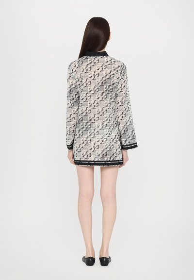 Rochie din dantelă cu un model abstract alb-negru, mâneci lungi și un guler negru. Bază tăiată cu un detaliu de franjuri ușor.