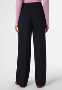 Hose mit weitem Bein aus dunkelblauem Stoff, der eine glatte Textur aufweist, seitliche Taschen hat und an der Taille tailliert geschnitten ist, ergänzt durch rote Schuhe.