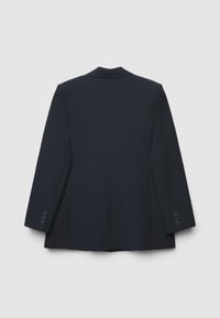 Blazer navy con uno spacco posteriore singolo, rever a punta e polsini a quattro bottoni. Il tessuto appare liscio, offrendo una silhouette strutturata e sartoriale.