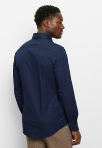 Navy blue long-sleeve shirt with a subtle dotted pattern, featuring a standard collar and buttoned cuffs, viewed from the back.