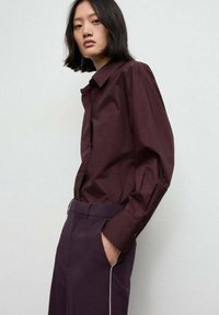 Bordeaux overhemd met knopen, gemaakt van textuurstof, met lange mouwen en een klassieke kraag, gecombineerd met donkere broek met witte bies.