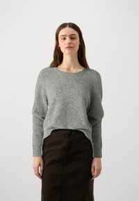Grå långärmad tröja med rundad halsringning, strukturerad tyg och avslappnad passform, i kombination med en mörkbrun jeanskjol.