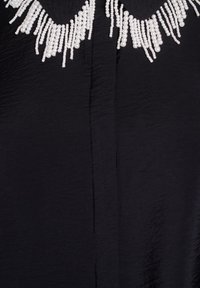 Tessuto nero con un colletto decorativo che presenta più fili di perle bianche appese a diverse lunghezze.