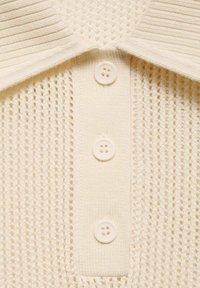 Strick-Polohemd in hellem Creme mit einem strukturierten Muster, kurzem geripptem Kragen und drei runden weißen Knöpfen an der Knopfleiste.