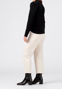 Musta pitkähihainen paita, off-white-housut ja mustat nilkkurit, joissa on massiivinen korko. Sujuvat kankaat ja räätälöity istuvuus näkyvät mallissa.