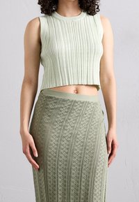 Lichtgroene geribde crop top, gecombineerd met een bijpassende kantgebreide rok met bloemmotieven en verticale strepen. Zachte textuur en aansluitend ontwerp.