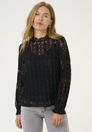 Black lace blouse with long sleeves, featuring a scalloped neckline, intricate patterns, and sheer fabric over solid inserts.