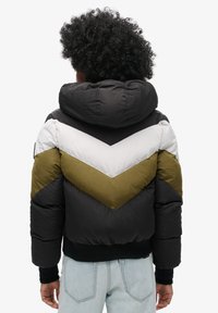 Pufferjacke met een zwarte body, olijfgroene en witte chevron-details, een oversized capuchon, geribbelde manchetten en een aansluitende pasvorm bij de taille.