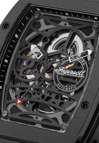 Zegarek automatyczny z przezroczystą czarną tarczą typu skeleton, srebrnymi zębatkami z purpurowymi akcentami oraz czerwonymi i białymi znacznikami godzinnymi.